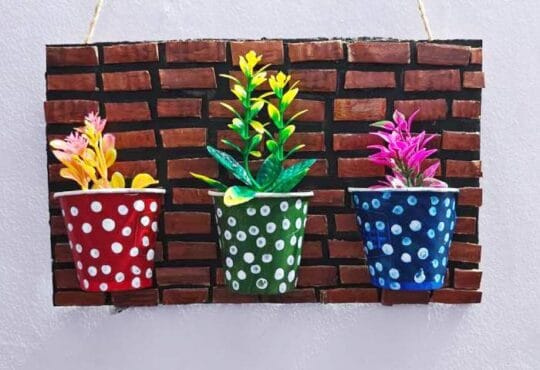 Colorful artificial flowers placed inside decorated paper cups mounted on a cardboard wall decor base, completing the DIY project