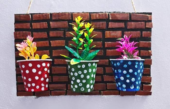 Colorful artificial flowers placed inside decorated paper cups mounted on a cardboard wall decor base, completing the DIY project