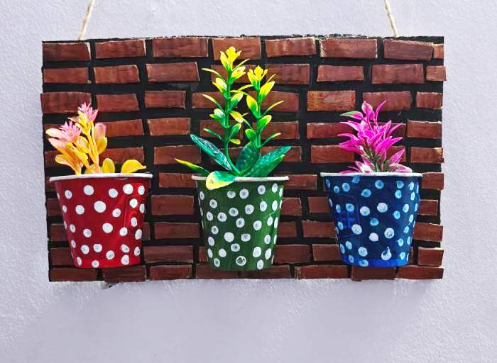 Colorful artificial flowers placed inside decorated paper cups mounted on a cardboard wall decor base, completing the DIY project