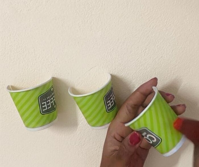 Hands shaping small green paper cups to prepare decorative elements for a DIY cardboard wall decor project