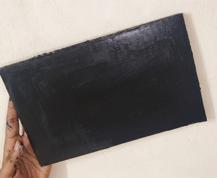 Hand holding a cardboard piece painted black to create the base for a DIY wall decor project